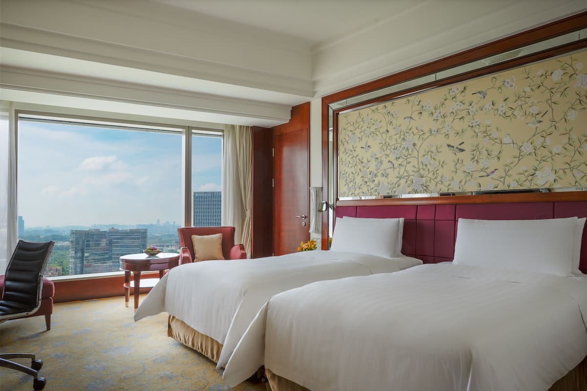 A hotel room with two beds, a view of the city, and a floral wall decoration.