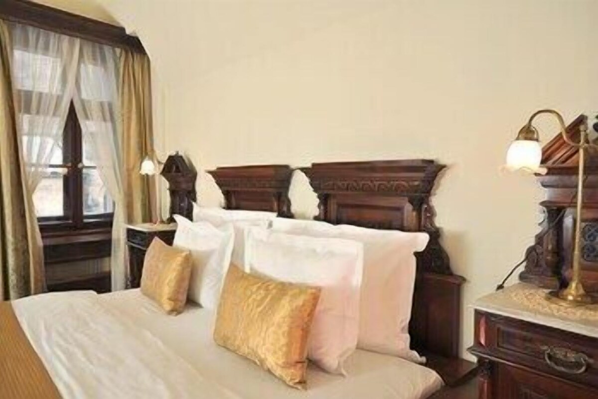 Una habitación de hotel con una cama, una mesita de noche, una lámpara y una ventana con cortinas.