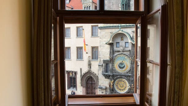 A view through a window of a building with a large, ornate clock and a door with intricate carvings. - Grand Hotel Praha (Prague)
