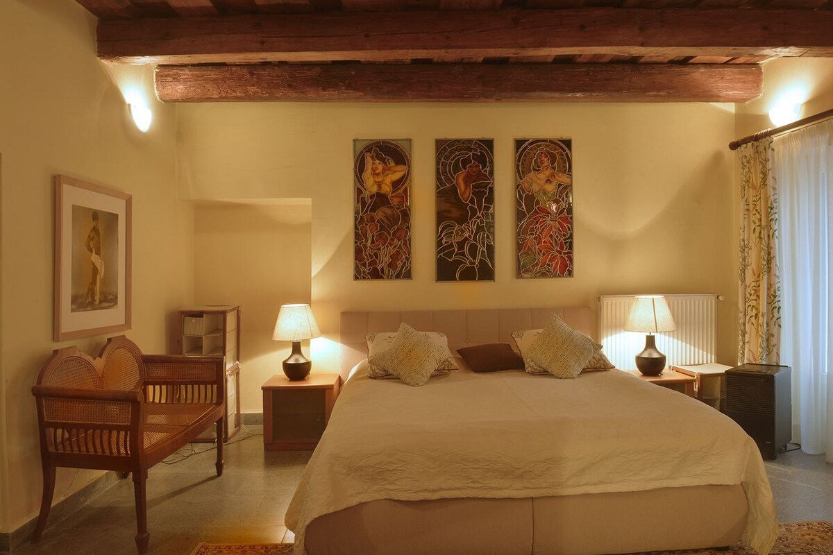 Un dormitorio con una cama grande, dos mesitas de noche con lámparas, una silla de madera y tres obras de arte colgadas en la pared.