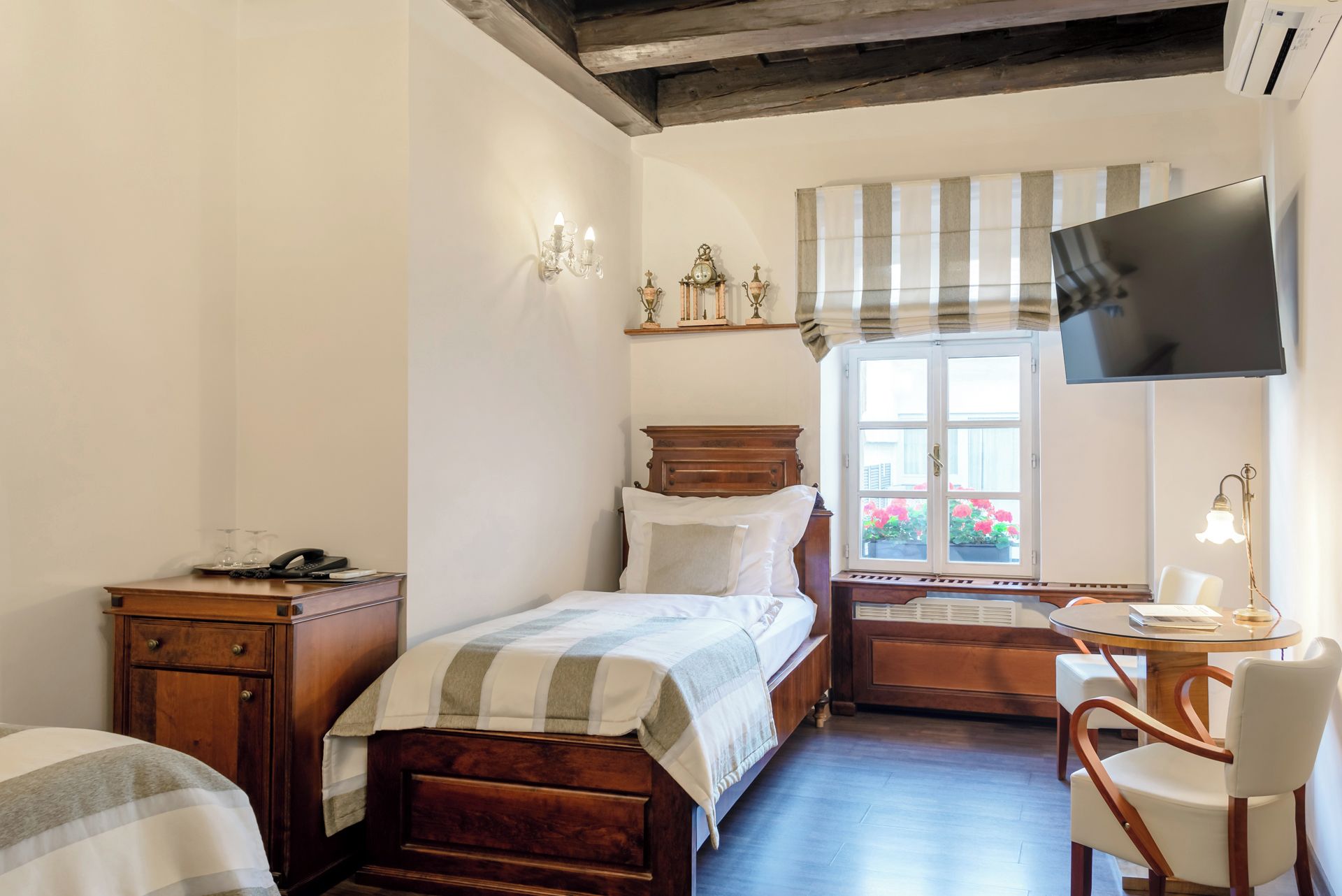 Un dormitorio con cama, mesita de noche, lámpara y televisor montado en la pared.