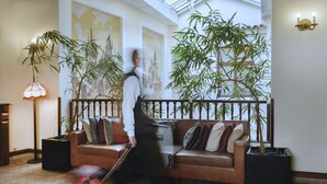 A hotel lobby with a brown leather sofa, a standing lamp, and large potted plants. - Grand Hotel Praha (Prague)
