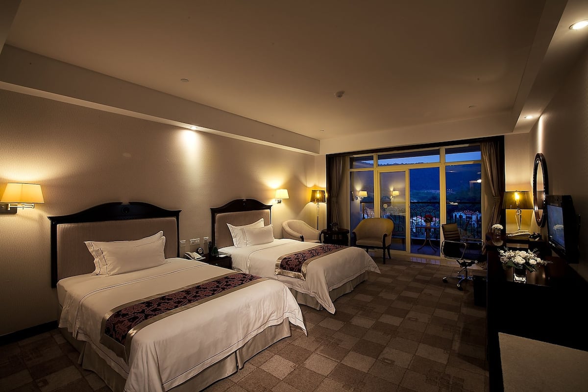 Ett hotellrum med två sängar, ett skrivbord, en stol och ett stort fönster med utsikt.