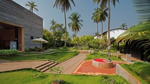 Un edificio moderno con fachada de ladrillo, un jardín bien cuidado con palmeras y un parterre circular de flores rojas.