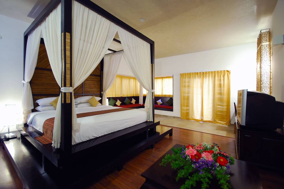 Una cama con dosel, ropa de cama blanca, un cabecero de madera y una mesita de noche con un florero.