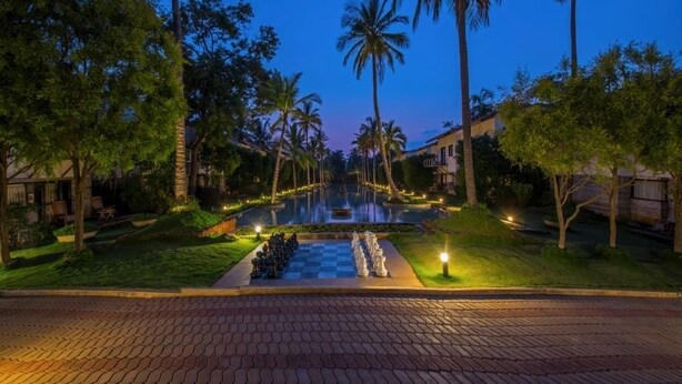 Un espacio exterior bien iluminado con piscina, palmeras y un diseño de cuadros en el suelo.