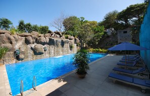 A swimming pool with a rock wall, lounge chairs, and a potted plant. - The Windflower Resorts and Spa (Mysore)