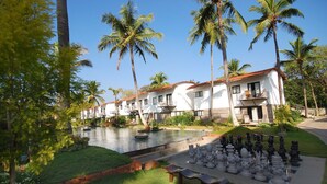 Un resort con varias edificaciones blancas, una piscina y un tablero de ajedrez en primer plano.