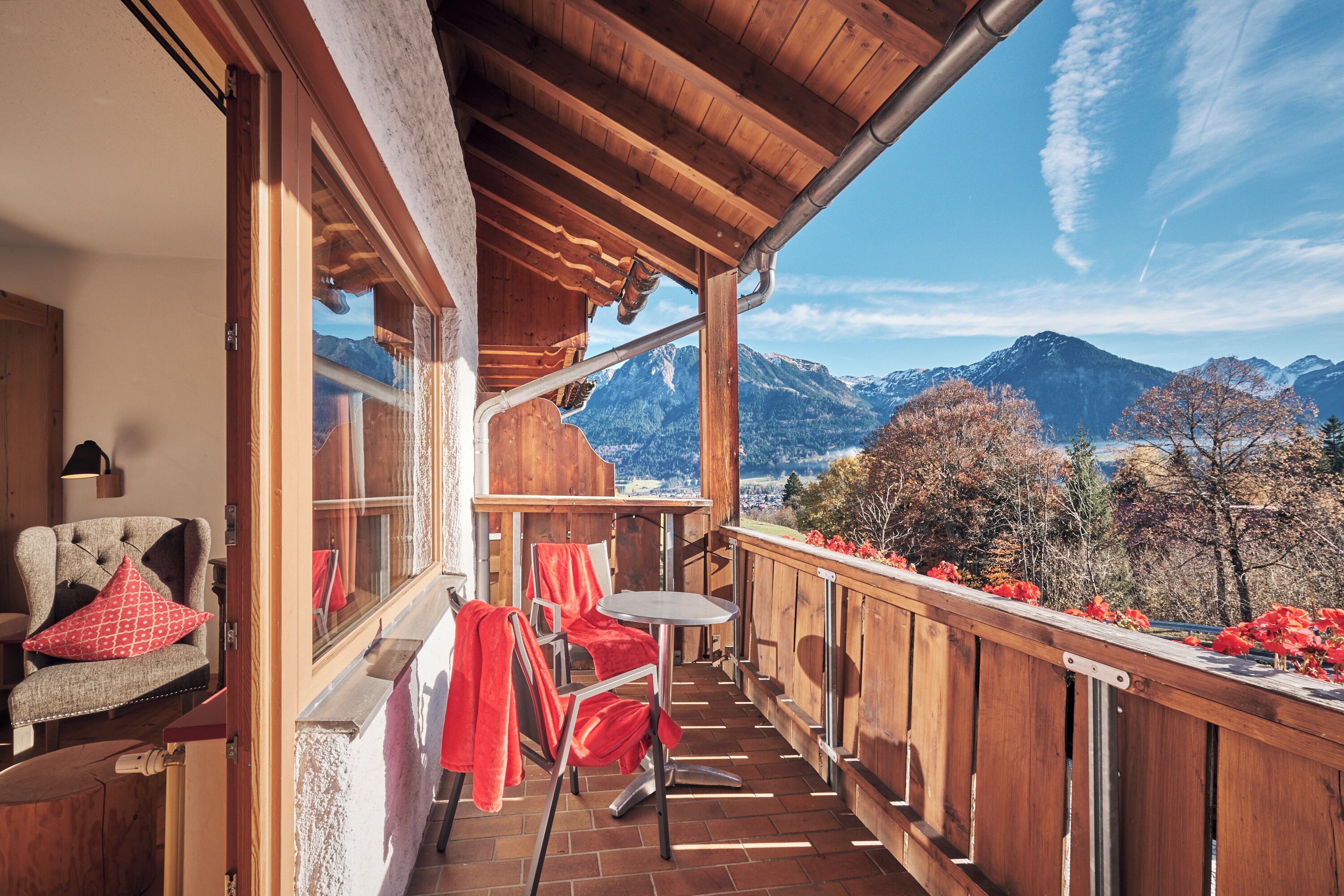 Un balcón de madera con vistas a montañas, una mesa y sillas.