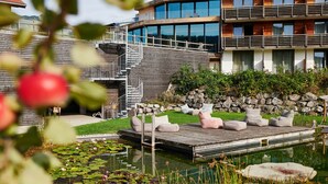 A modern building with a wooden deck, a stone wall, and a pond with lily pads. - Hotel Oberstdorf (Oberstdorf)