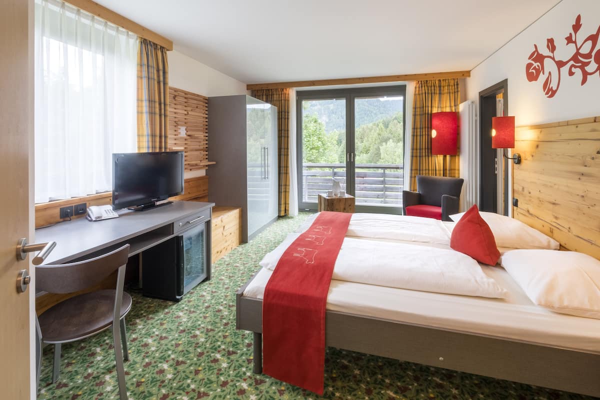 Une chambre d’hôtel avec un lit, un bureau avec une télévision, une chaise et une fenêtre avec des rideaux.