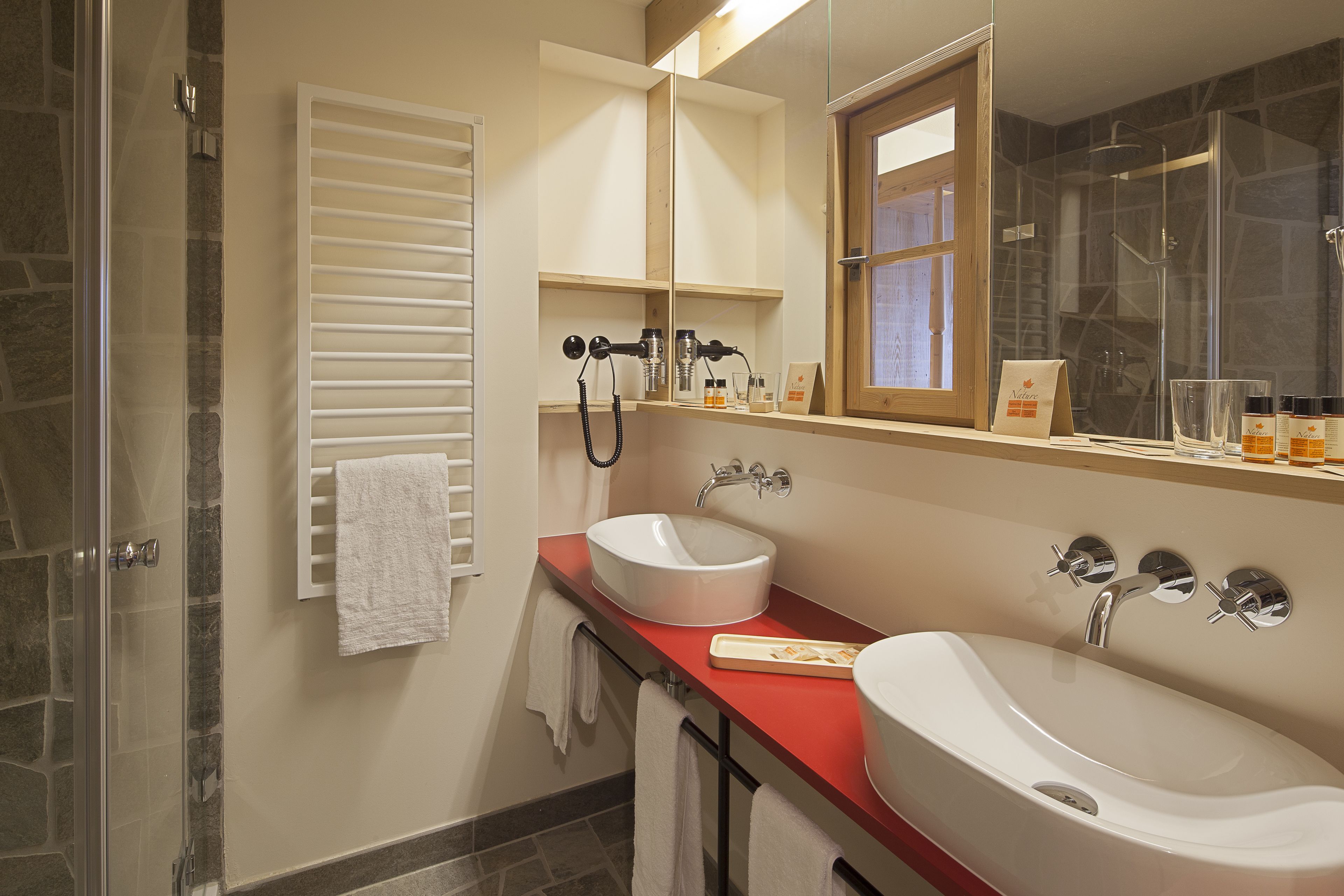 Un baño con cabina de ducha de vidrio, dos lavamanos y un espejo con marco de madera.