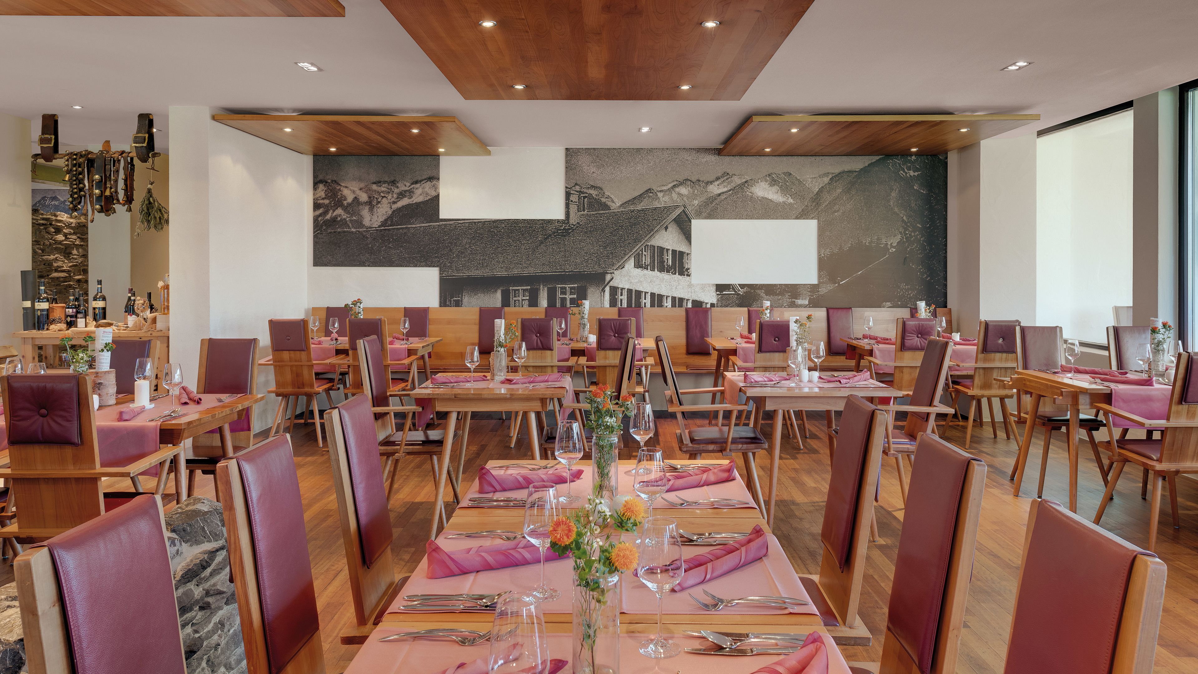 A restaurant with wooden tables and chairs, a mountain mural on the wall, and a bar area with bottles.