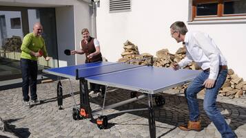 Ein Pingpongtisch auf einem Kopfsteinpflasterplatz, im Hintergrund ein weißes Gebäude.