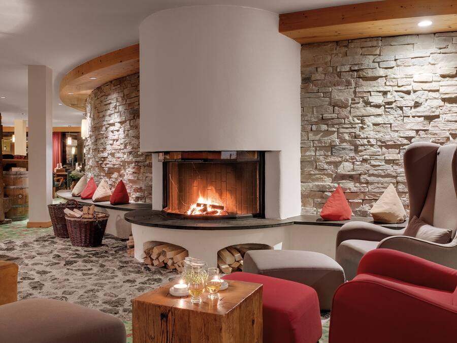 A cozy lounge area with a stone fireplace, comfortable seating, and a rustic wooden ceiling.