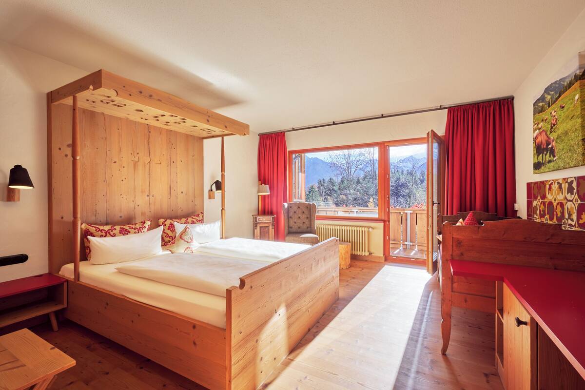 Un lit en bois donnant sur les montagnes, une chaise rouge et un bureau en bois.