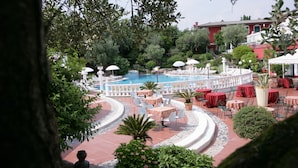 Un espace aménagé au bord de la piscine, avec des tables et des chaises, entouré de verdure et avec un bâtiment rouge en arrière-plan.