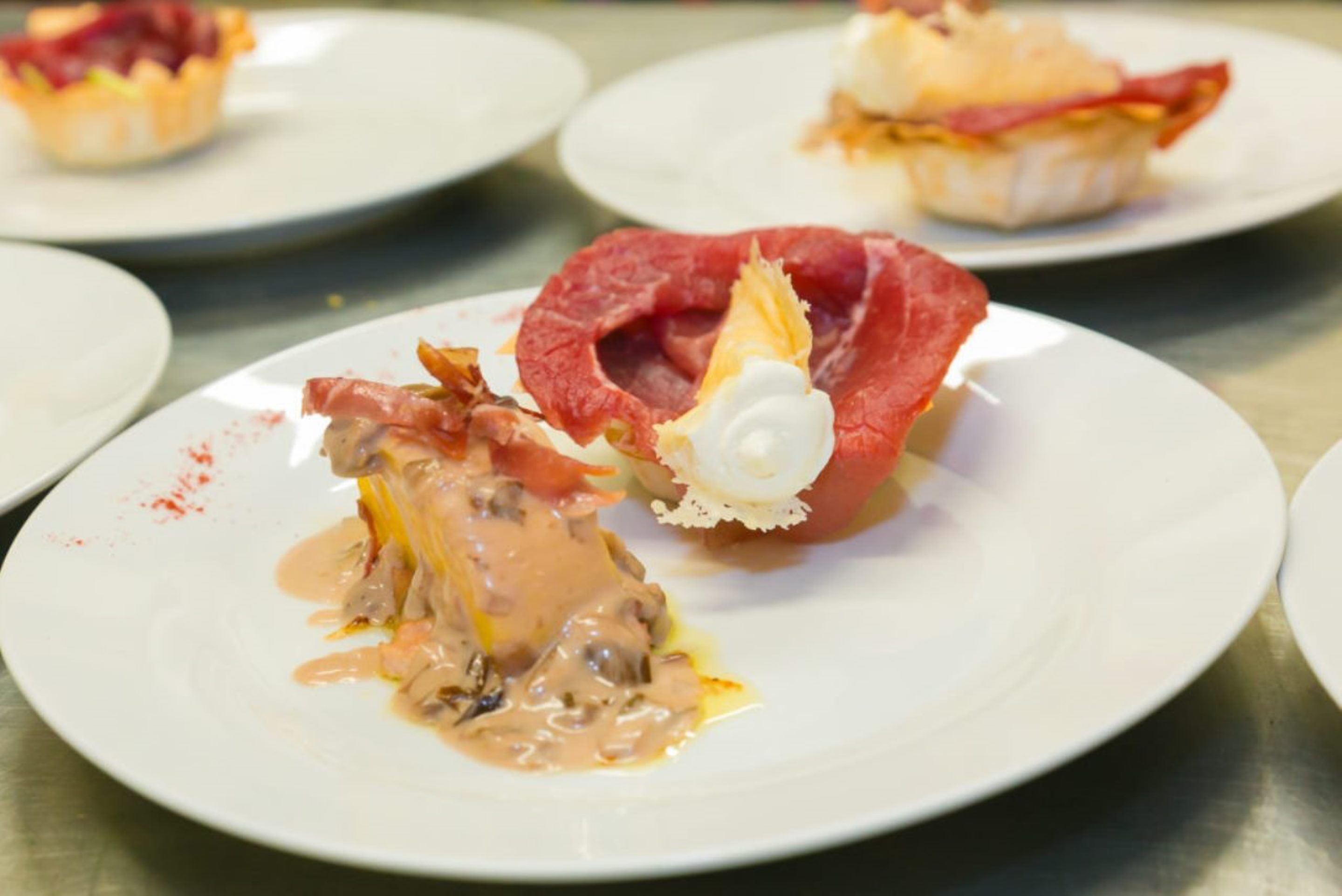 Un plato de postre con salsa cremosa y un trozo de carne roja, posiblemente filete, sobre un plato blanco.