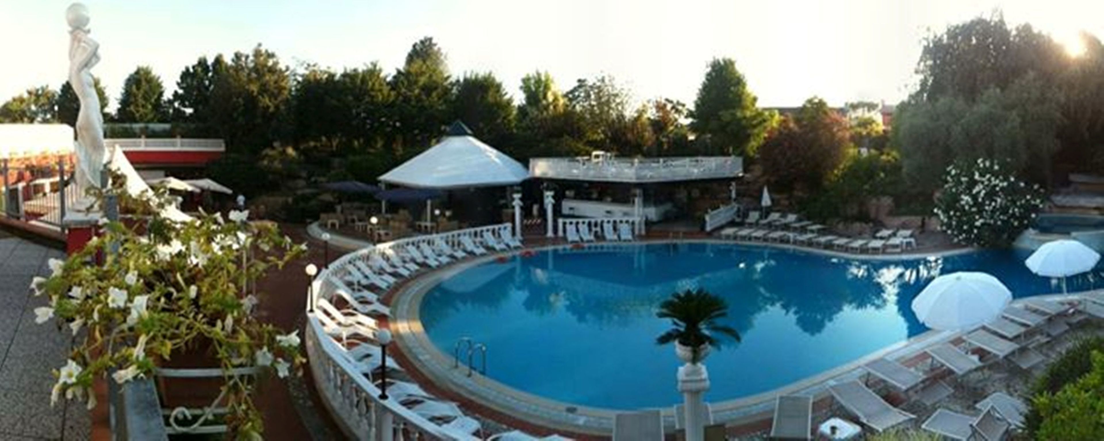 A swimming pool with lounge chairs and umbrellas, surrounded by trees and a statue.