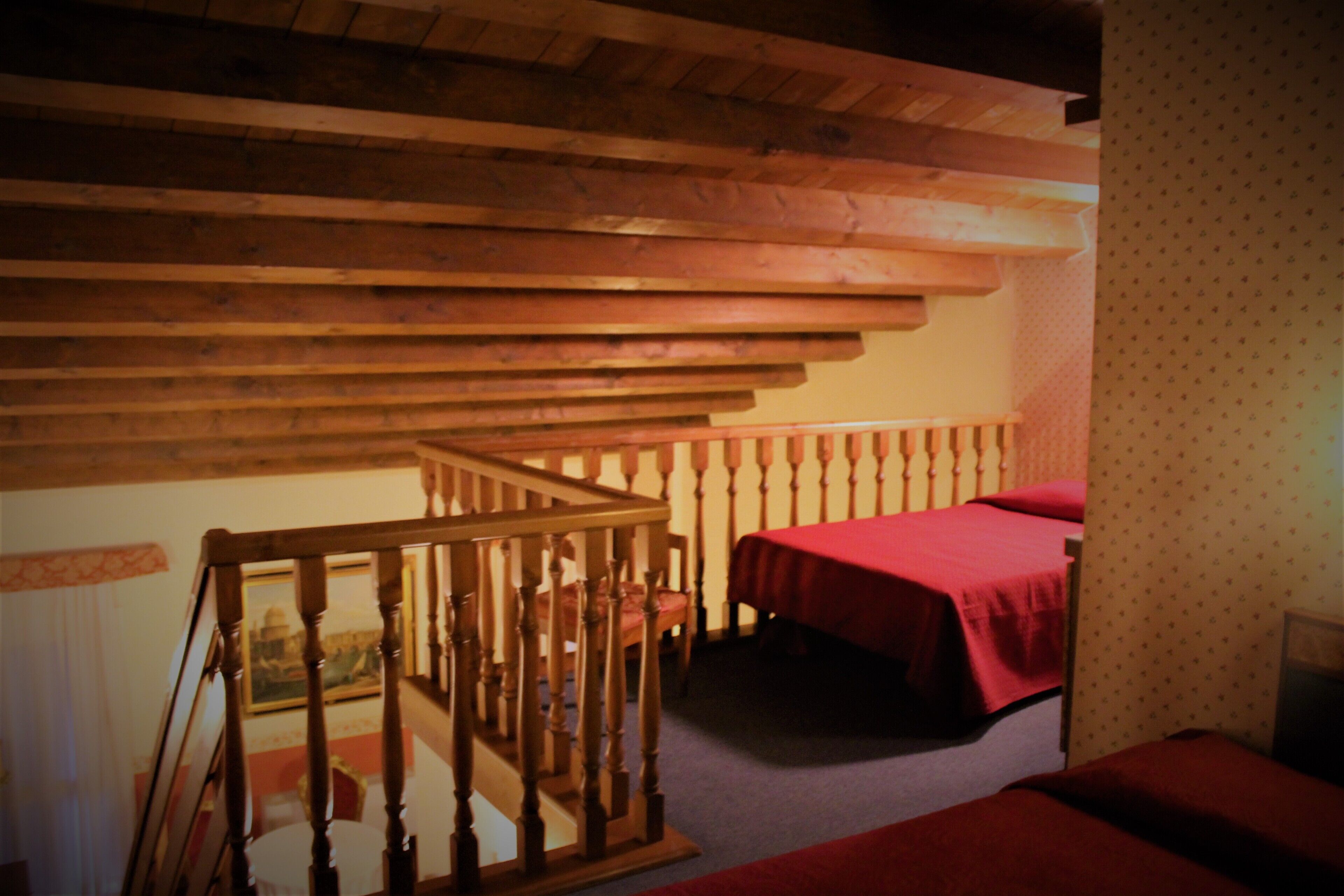A room with a wooden staircase, a bed with a red bedspread, and a patterned wall.