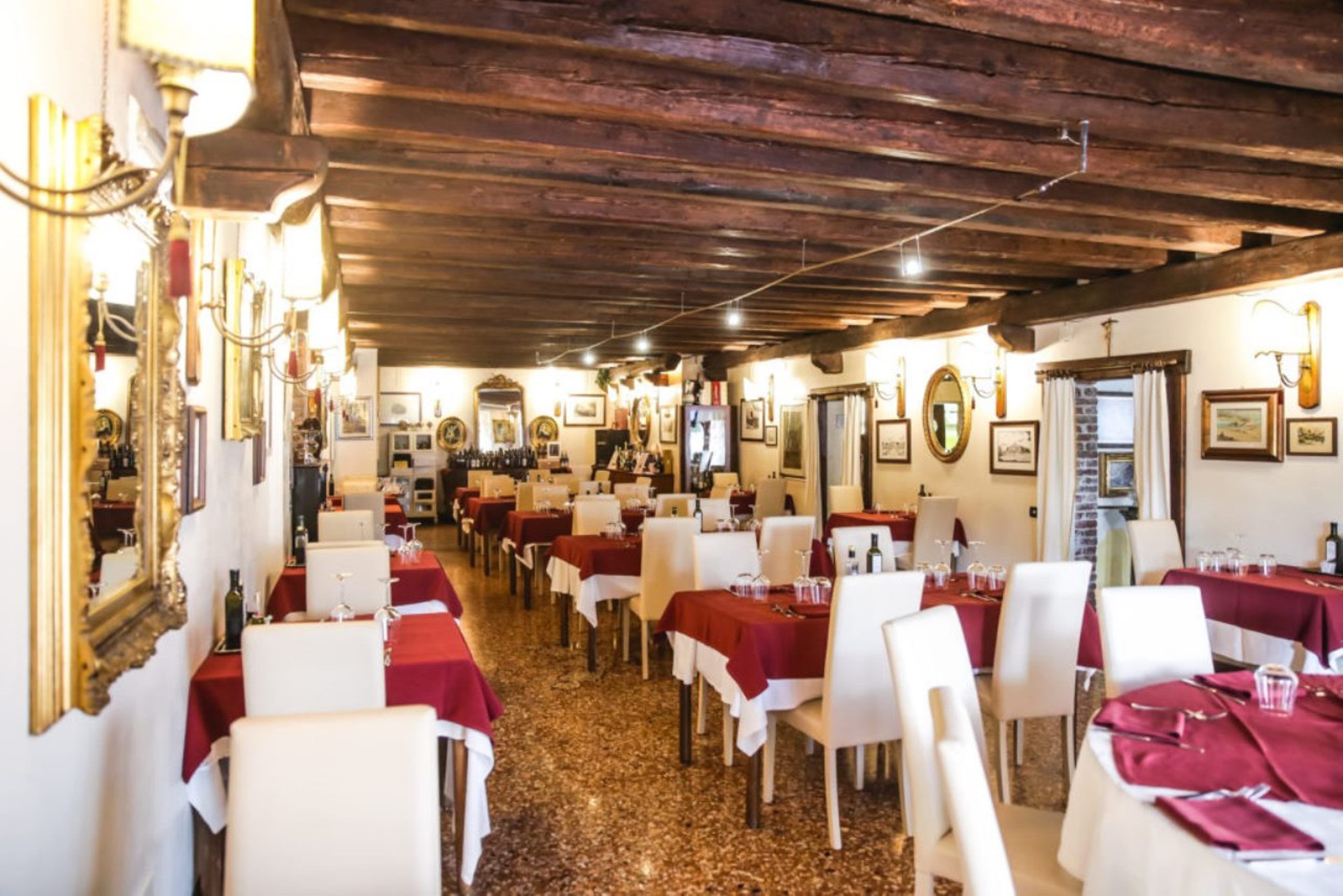 Ein Restaurant mit mehreren Tischen, weißen Stühlen und roten Tischdecken.