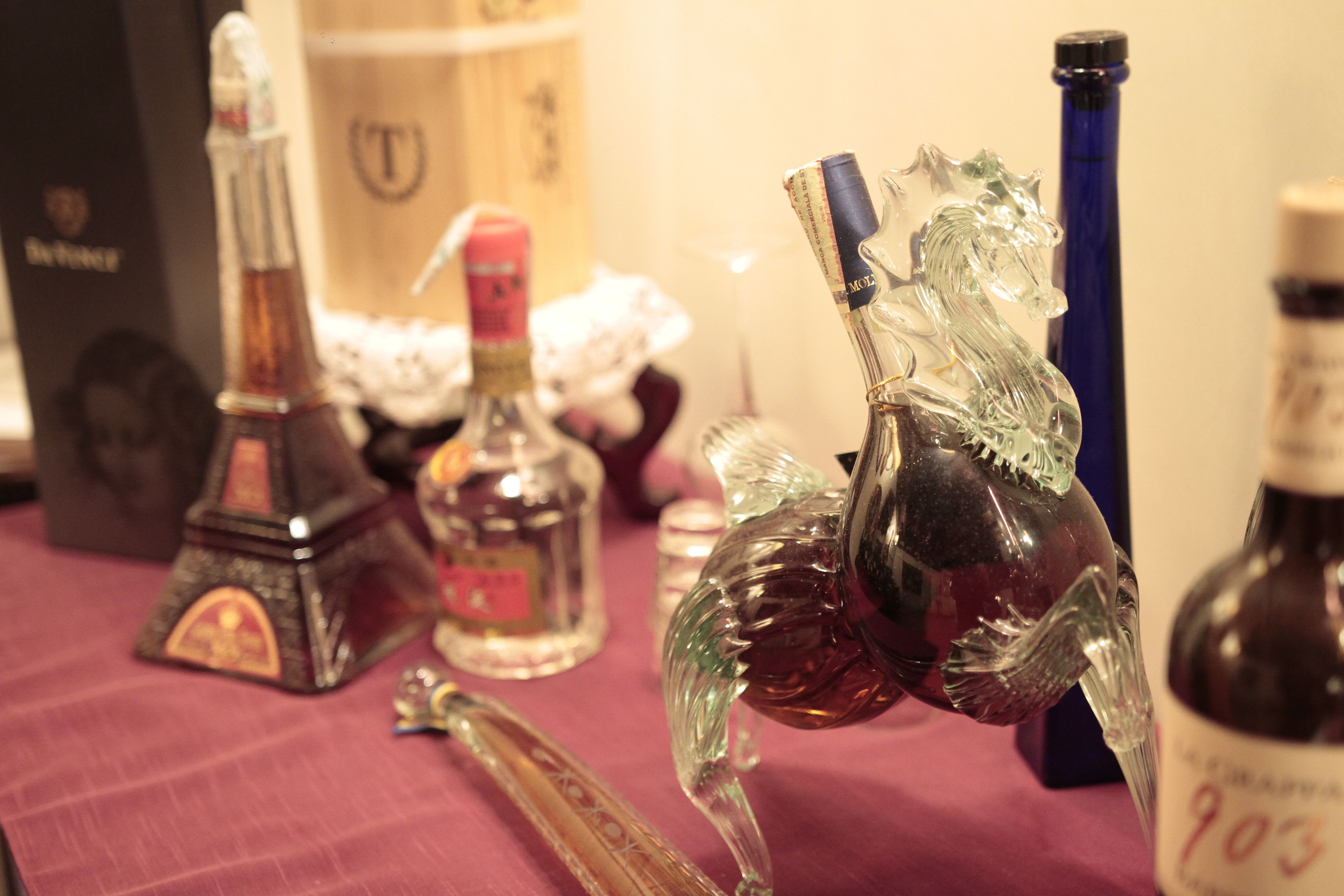 A table with various glassware and bottles, including a decorative glass horse and a bottle with a label.