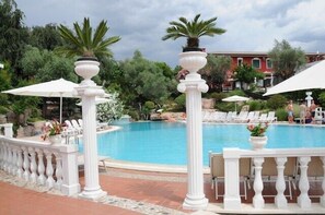 Een zwembad met witte balustrades, ligbedden en parasols.