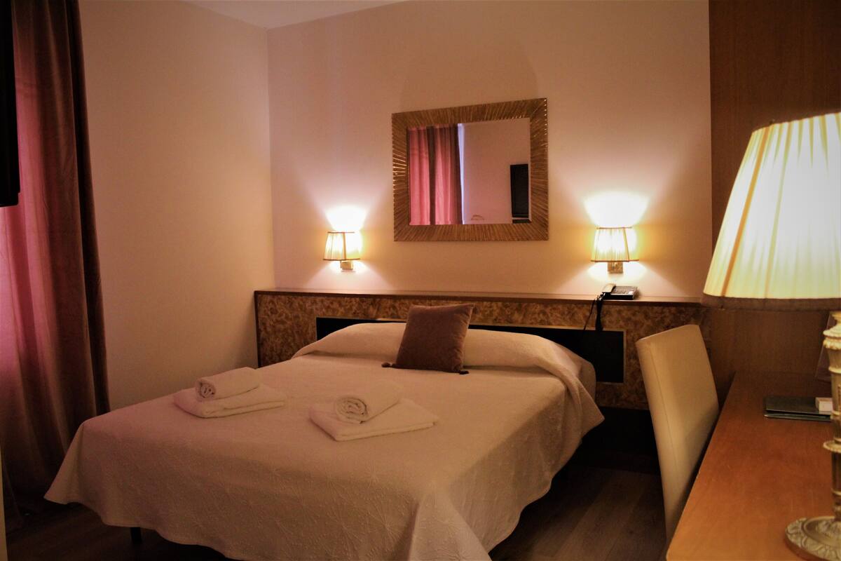 Une chambre d’hôtel avec un lit, deux lampes de chevet, un miroir, une chaise et une table.