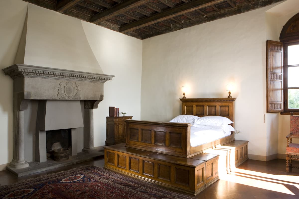 A bedroom with a large bed, a fireplace, and a window.