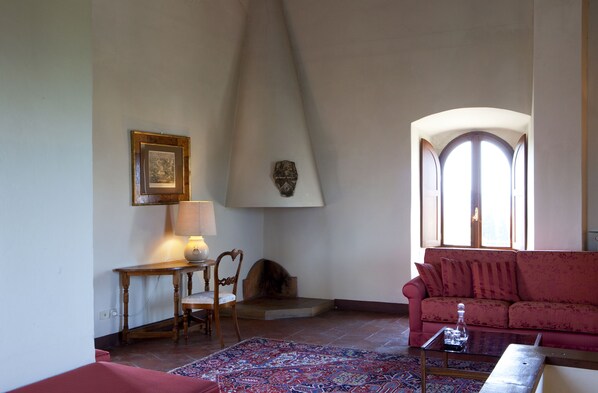 A living room with a red sofa, a wooden table with a lamp, a patterned rug, and a fireplace.