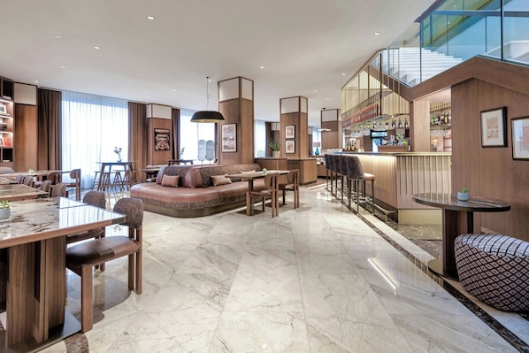 A spacious hotel lobby with a central seating area, a bar, and a staircase leading to an upper level. - AC Hotel Milano by Marriott (Milan)