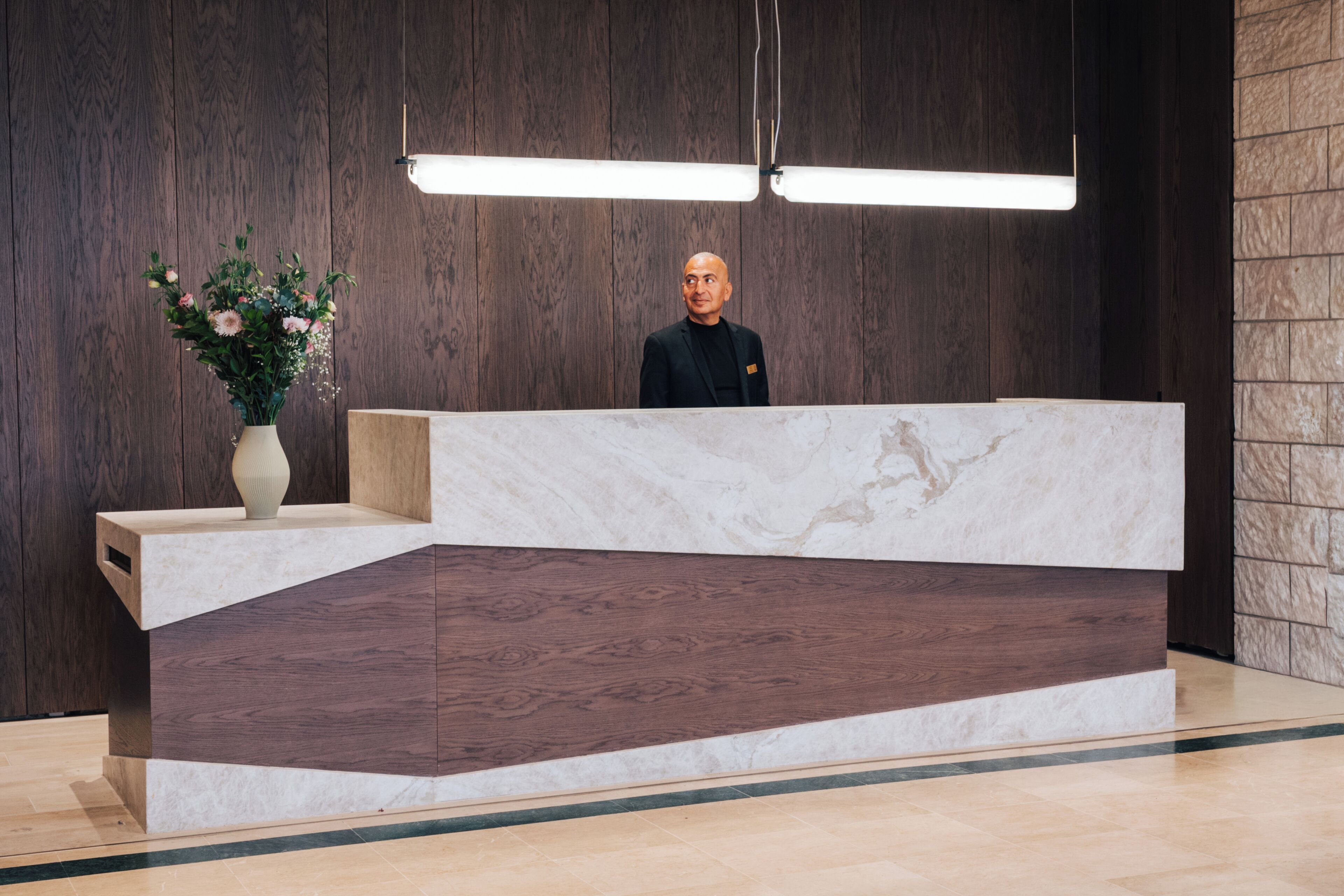 A reception desk with a marble top, wooden paneling on the walls, and a vase of flowers on the left.