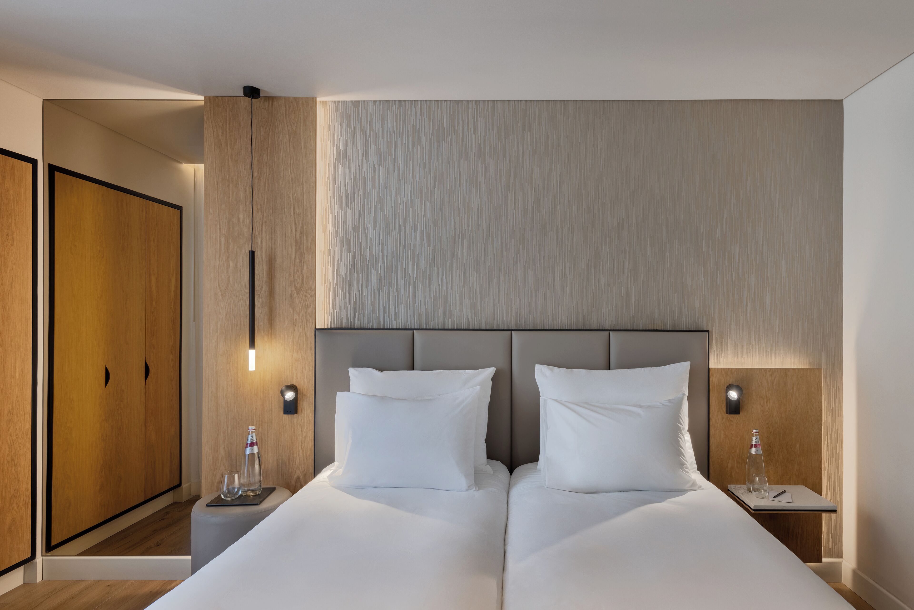 A modern hotel room with a large bed, two bedside tables, and a wardrobe.