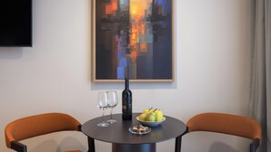 A modern dining area with a round table, two orange chairs, a black bottle, and a fruit bowl. A colorful abstract painting hangs above the table. - Skyline Hotel Jerusalem (Jerusalem)