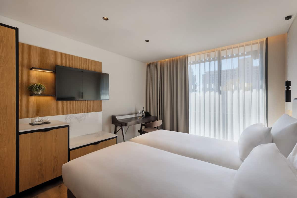 Une chambre d’hôtel moderne équipée d’un lit, d’un bureau, d’une télévision et d’une fenêtre avec des rideaux.