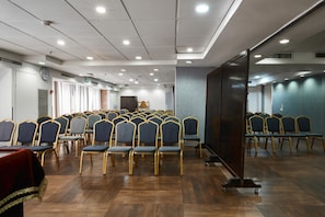 Ein Konferenzraum mit Tischen und Stühlen, einer Uhr und einer großen Leinwand.