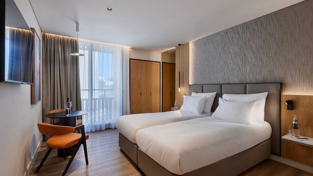 A modern hotel room with a large bed, a desk with a chair, a TV, and a view of the city. - Skyline Hotel Jerusalem (Jerusalem)