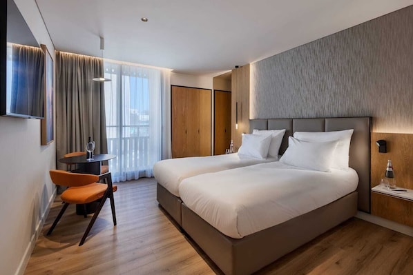 Ein modernes Hotelzimmer mit einem großen Bett, einem Schreibtisch mit Stuhl, einem Fernseher und Blick auf die Stadt.