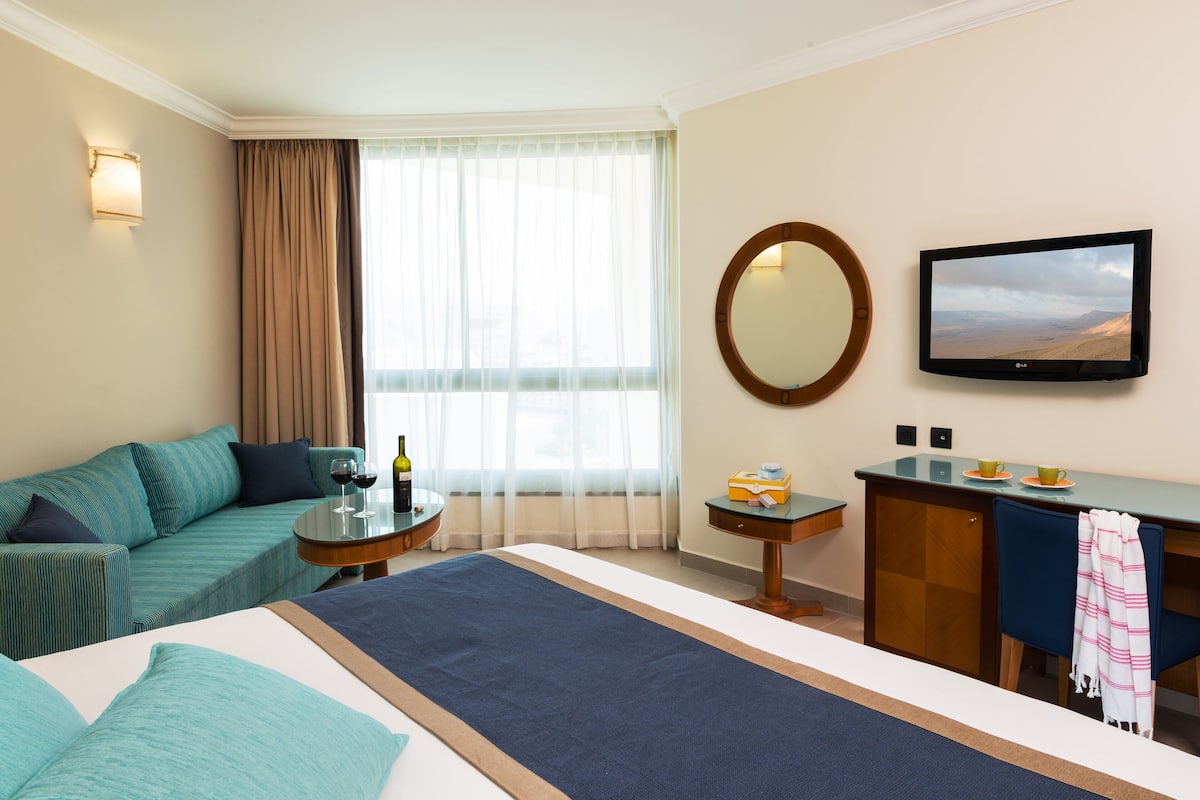 A hotel room with a bed, a sofa, a desk, a television, and a window with curtains.