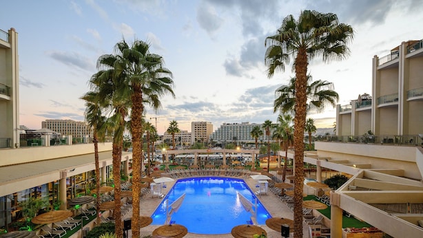 A rooftop pool area with palm trees, lounge chairs, and a view of the city skyline. - U Magic Palace Hotel (Eilat)