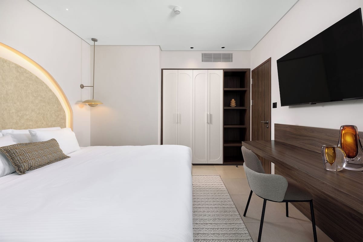 A modern hotel room with a bed, a desk, a chair, a TV, and a wardrobe.
