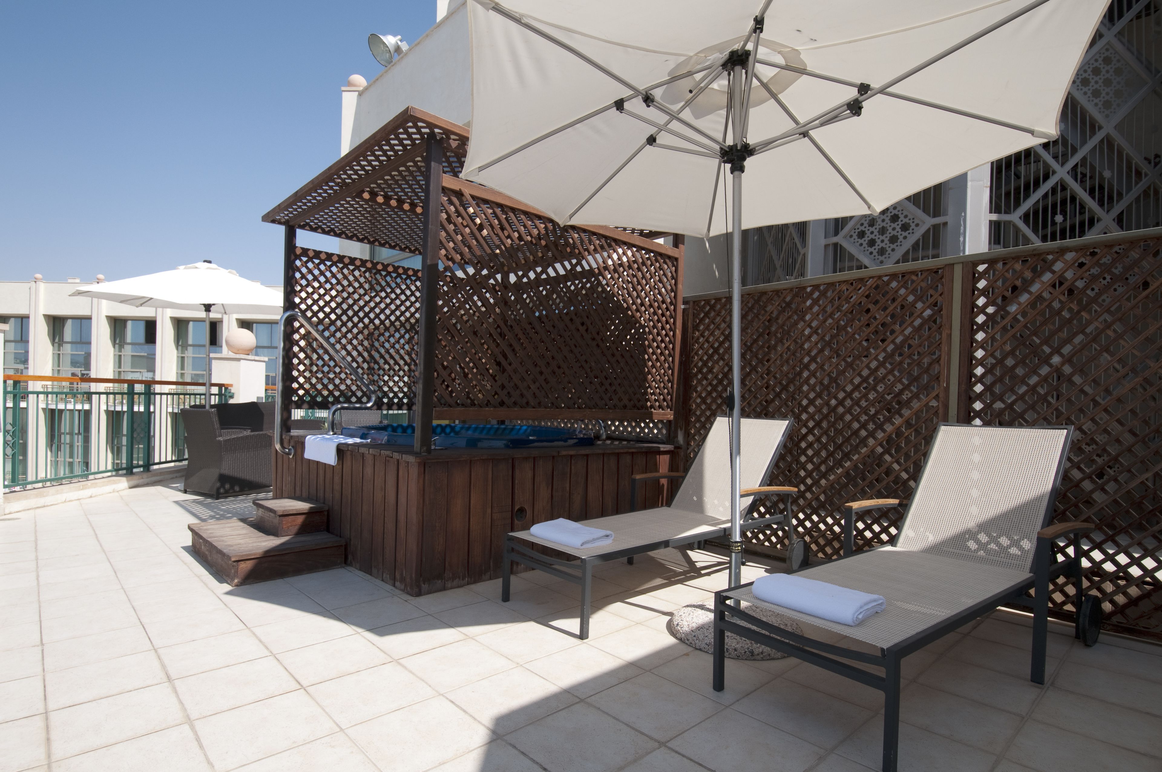 Eine Terrasse im Freien mit einem Holzkohlegrill, zwei Liegestühlen und einem großen Sonnenschirm.