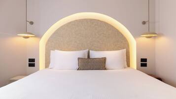 Una cama impecable con ropa de cama blanca y un almohadón texturizado, flanqueada por dos lámparas de pared.
