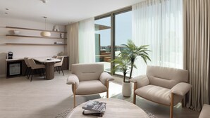 A modern living room with a dining area, a large window with curtains, a potted plant, and a sofa. - U Magic Palace Hotel (Eilat)