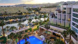 A hotel with a pool area, palm trees, and a view of a marina and cityscape. - U Magic Palace Hotel (Eilat)