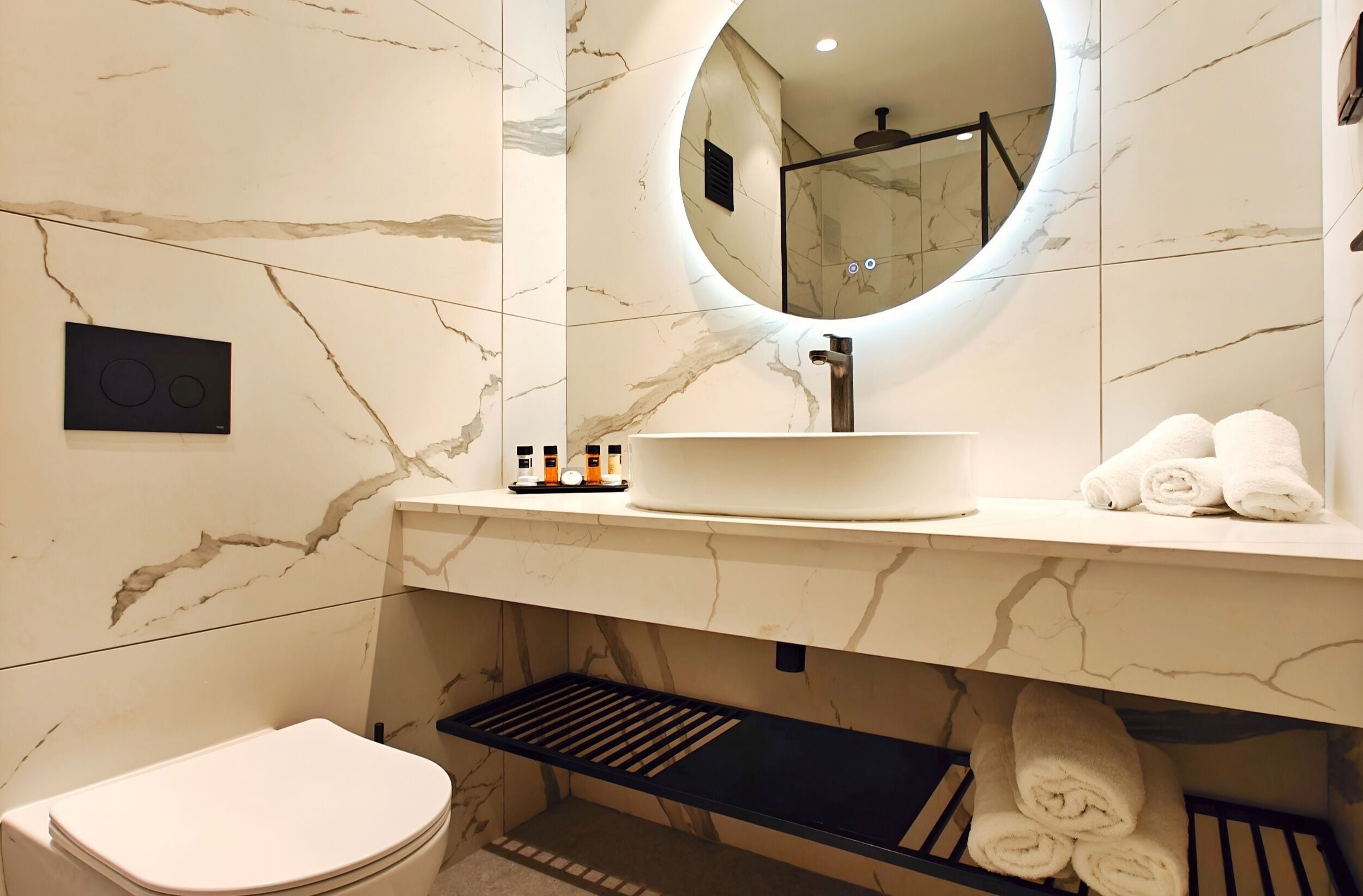 Ein Badezimmer mit Marmorwaschtisch, rundem Spiegel, Toilette und Handtuchhalter.