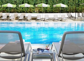 Une vue sur la piscine, avec des chaises longues, des parasols et une boisson sur une table.