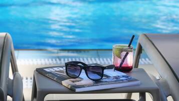 A pair of sunglasses, a drink with a straw, and a magazine on a chair by a pool.