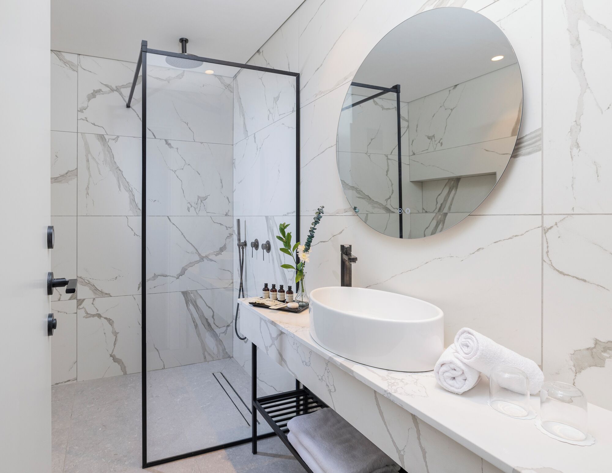 Un baño moderno con ducha envuelta en vidrio, un lavamanos blanco y un espejo grande.