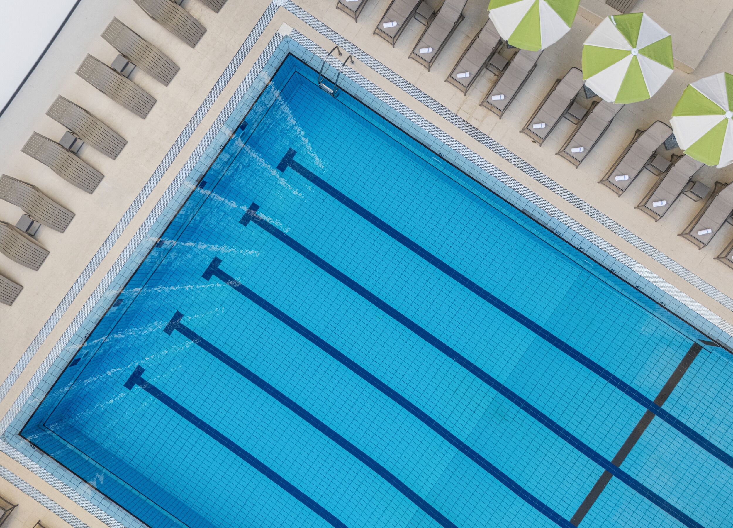 Una amplia piscina cubierta con varias pistas, rodeada de sillones de descanso y sombrillas.